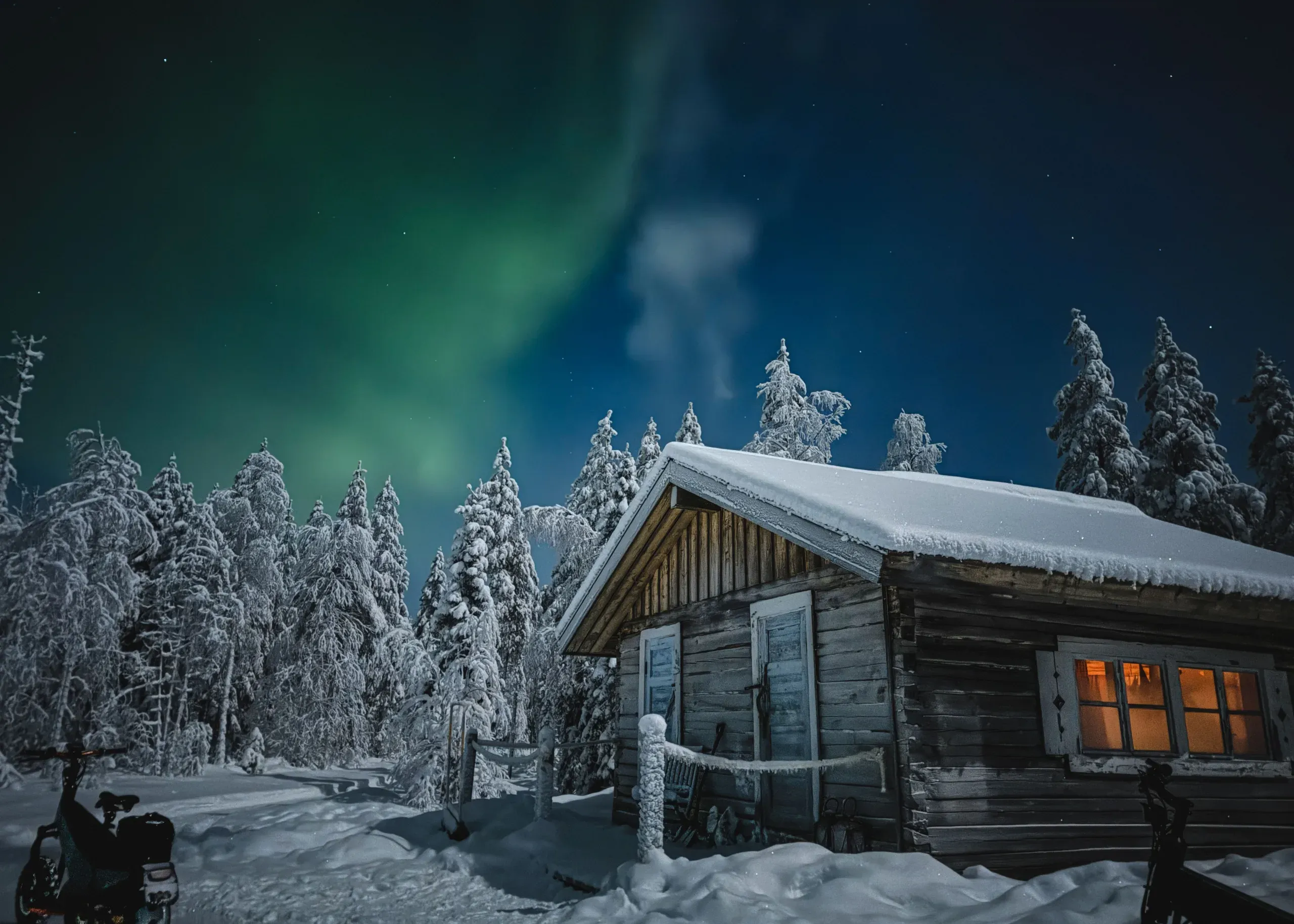 A green aurora over a snow-roofed log cabin with warm light in its windows, surrounded by heavily frosted spruce under a clear starry sky